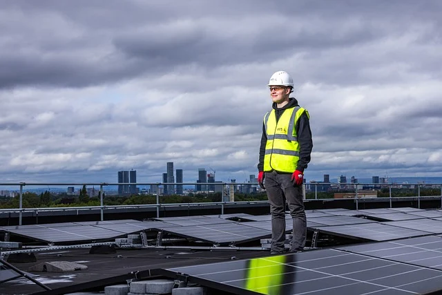 Un technicien sur un toit équipé de panneaux solaires, portant un casque et un gilet de sécurité.