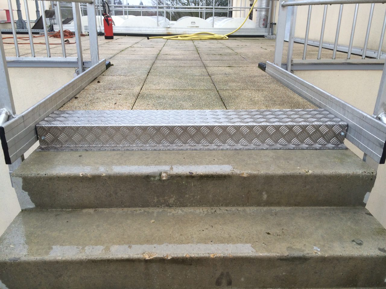 Installation d’un habillage de marche en aluminium sur terrasse extérieure Habillage de marche en aluminium antidérapant installé sur des escaliers en béton, avec un garde-corps métallique sur les côtés, sur une terrasse extérieure.