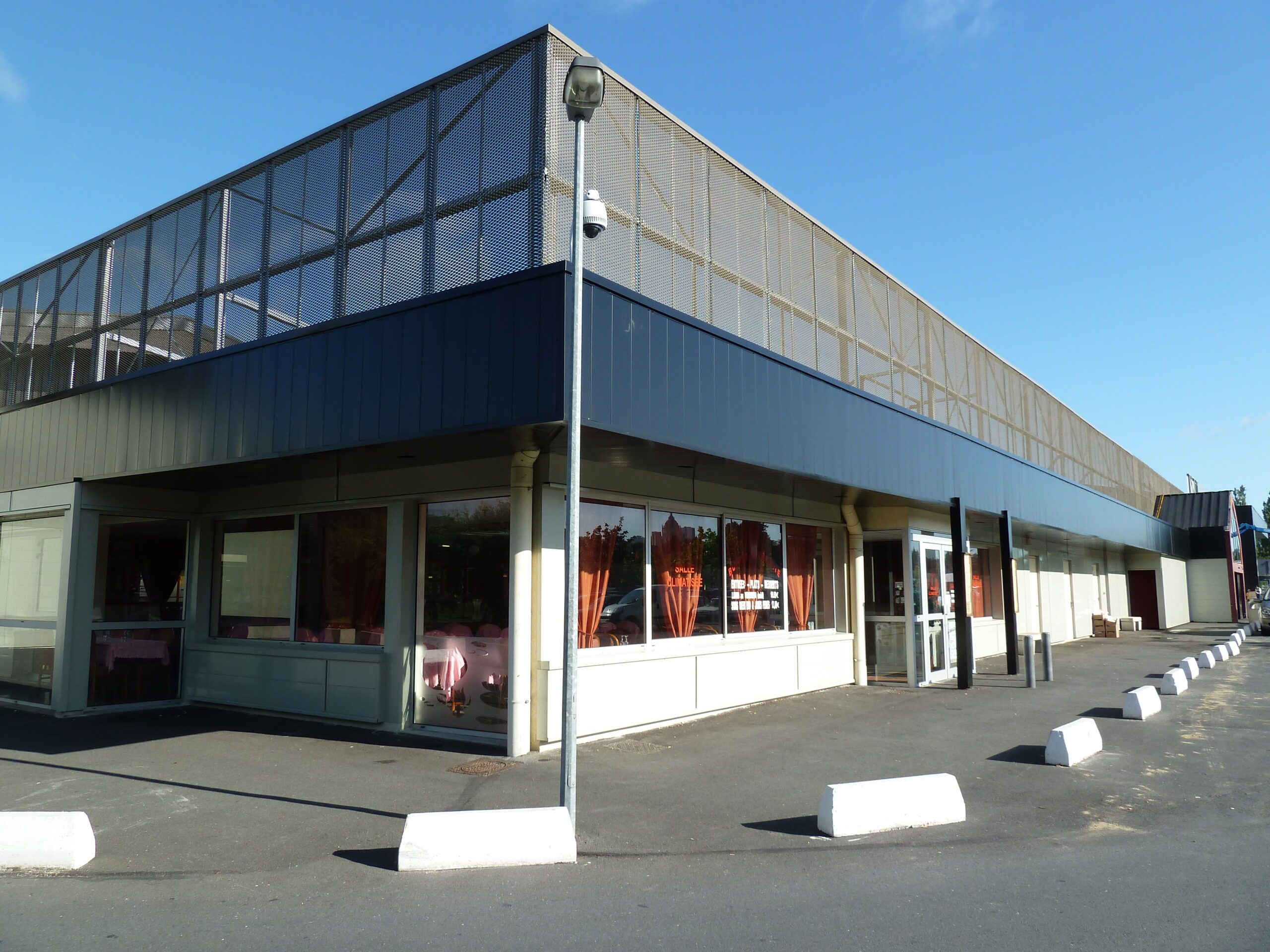 Relookage de la façade d’un centre commercial en bardage rapporté métallique avec pare-soleil ajouré Façade rénovée d’un centre commercial avec bardage métallique et parement décoratif ajouré